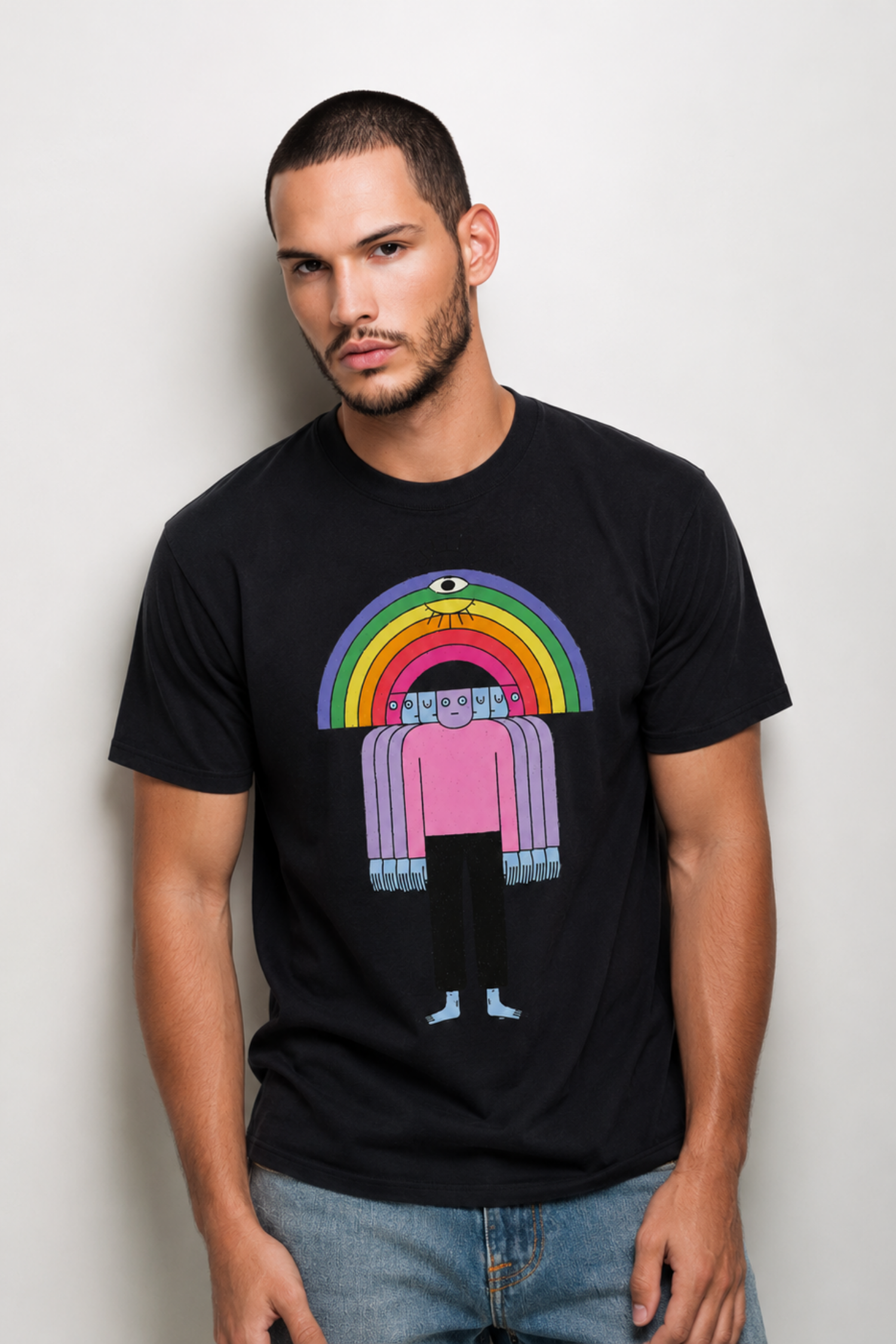 Male model wearing the Friends Tee by Del Lago Greenwich, featuring a colorful rainbow character graphic on a black t-shirt. Studio lifestyle image showcasing the fit and front graphic design.