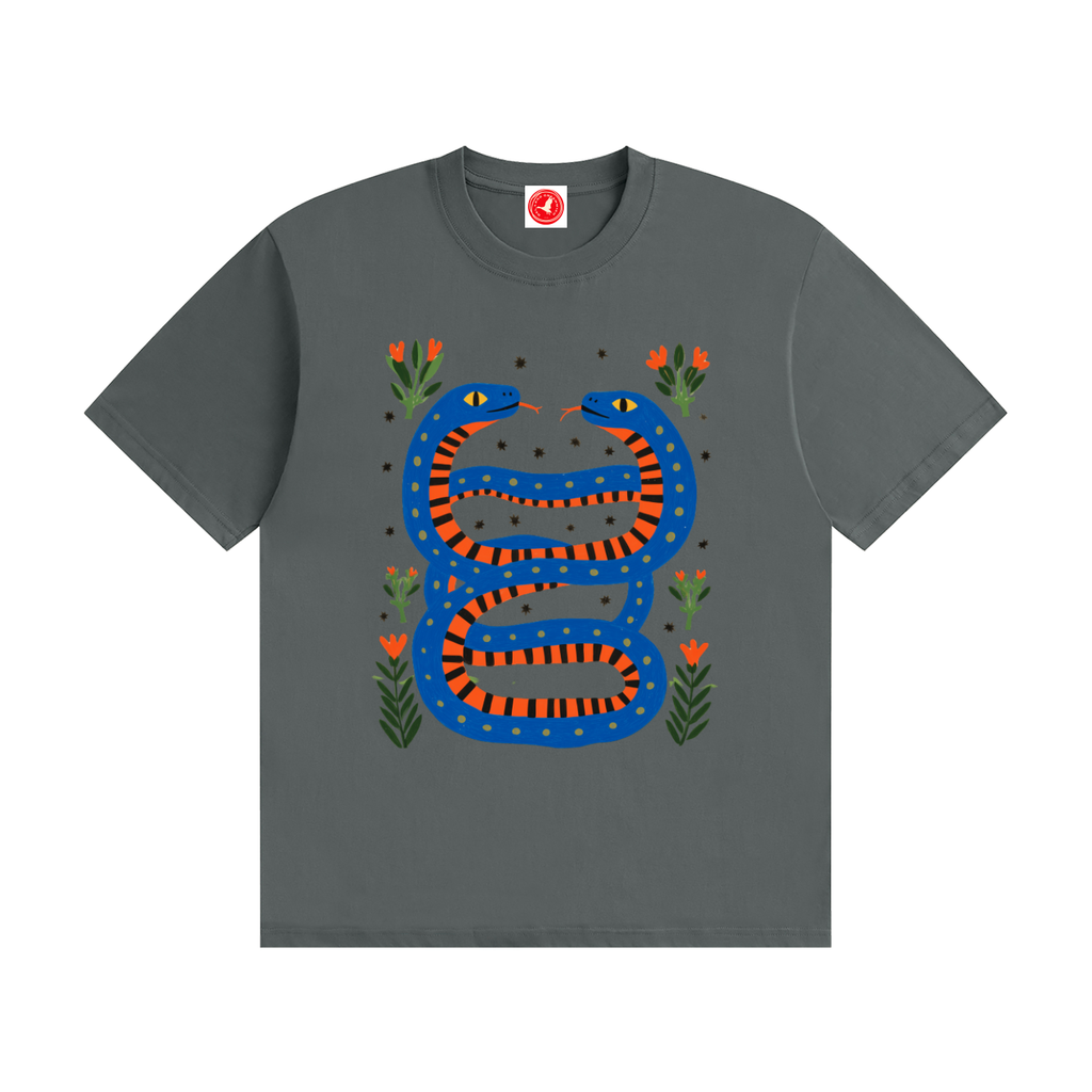 Twin Serpents boys graphic t-shirt featuring original blue and orange serpent artwork with floral accents. Soft cotton short-sleeve tee laid flat on a white background by Del Lago Greenwich.