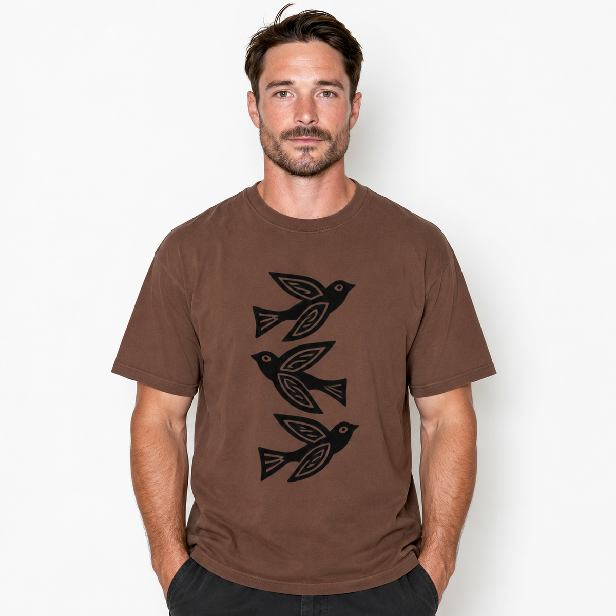 A man wearing a brown short-sleeve t-shirt with a black graphic of three stylized birds, set against a plain light gray background.