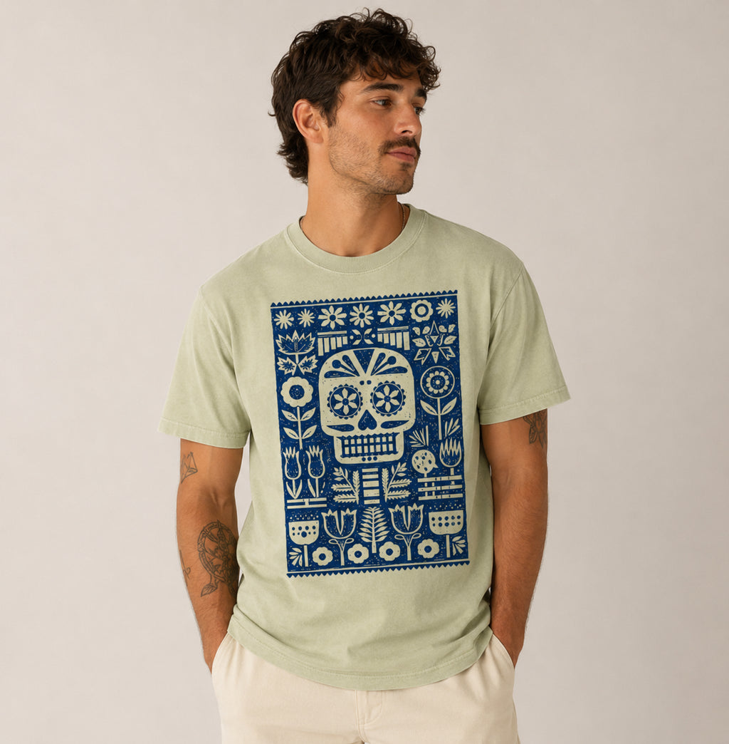 Man wearing a light greenFolk Skull graphic t-shirt featuring decorative skull artwork inspired by folk art and vintage illustration.