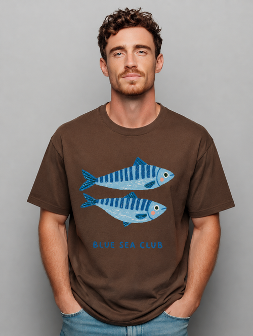 Man wearing a brown Blue Sea Club graphic t-shirt featuring coastal-inspired artwork celebrating ocean adventures and seaside living.