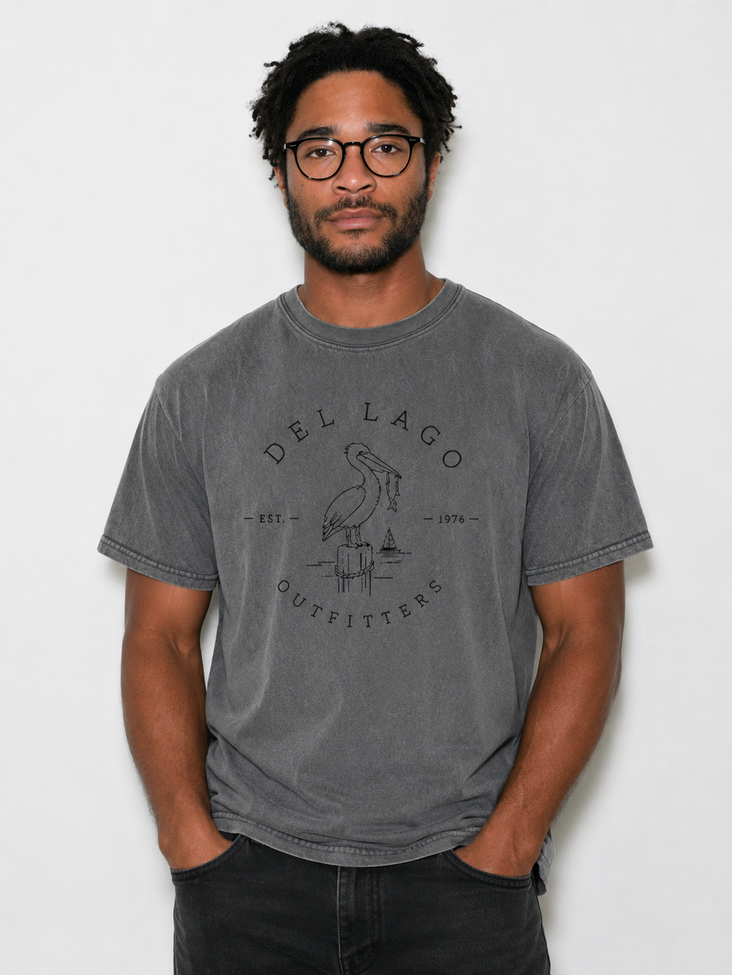 A man wearing a dark gray washed t-shirt with a black graphic print of a pelican and the text 'DEL LAGO OUTFITTERS'.
