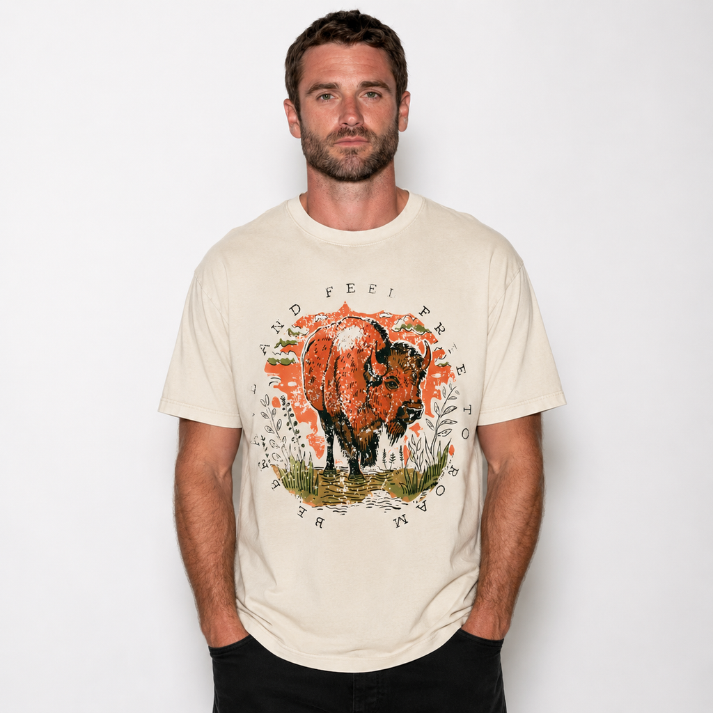 A man wearing a cream-colored graphic t-shirt with a stylized illustration of a cow and the text 'I'D FEEL FREE' on the front, set against a plain white background.