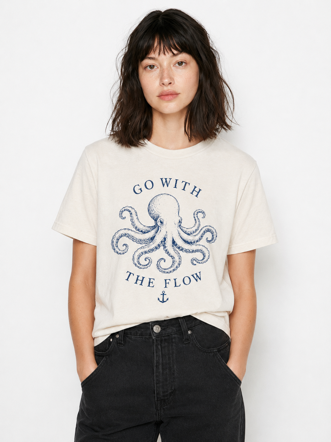 A woman wearing a cream-colored t-shirt with a blue octopus graphic and the text 'GO WITH THE FLOW', paired with black jeans, against a plain white background.