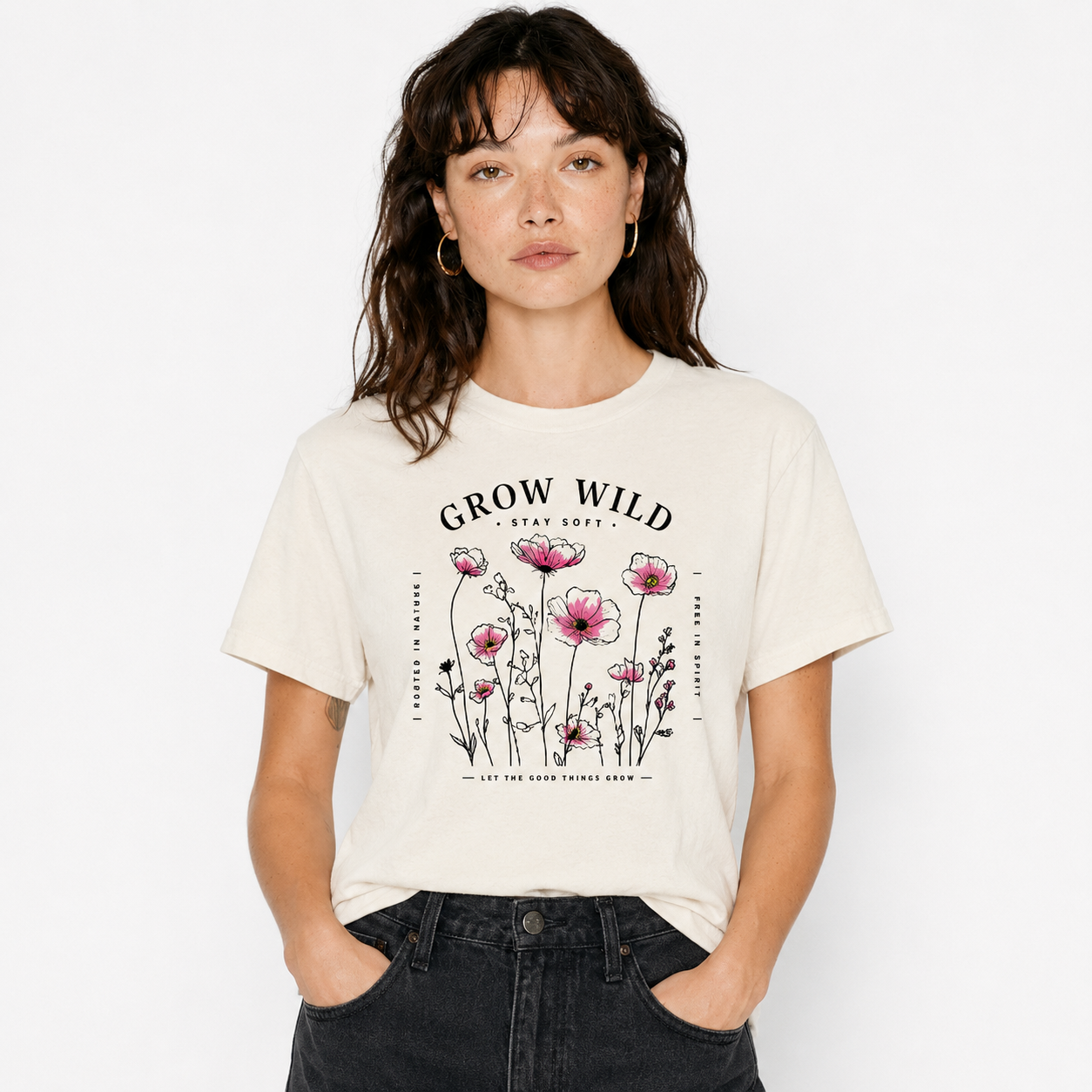 A woman wearing a cream-colored graphic t-shirt with a pink flower design and the text 'GROW WILD STAY LOOSE' on the front, paired with dark gray jeans, against a plain white background.