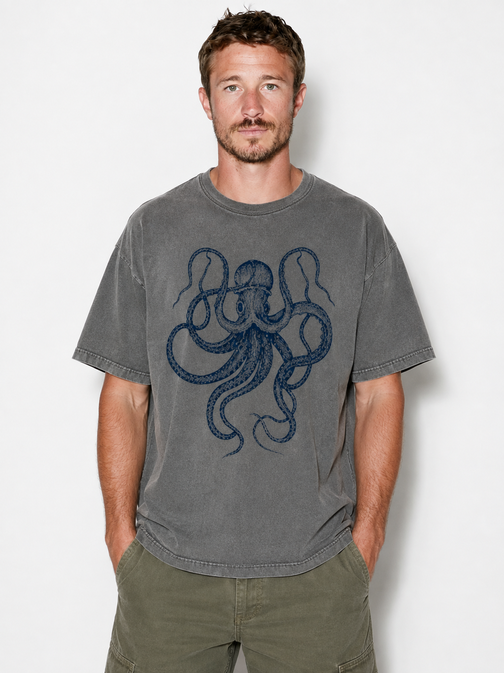 A man wearing a gray washed t-shirt with a dark blue octopus graphic on the front, paired with olive green cargo pants, standing against a light gray background.