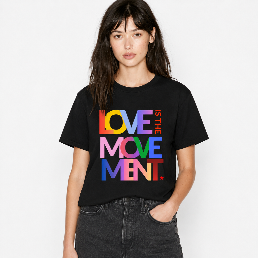 A woman modeling a black short-sleeve t-shirt with a colorful graphic text print reading 'LOVE IS THE MOVE MENT' in rainbow colors, paired with dark gray jeans against a plain white background.