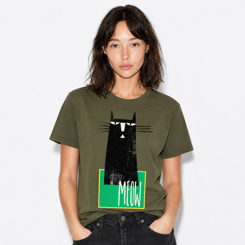 A woman wearing an olive green graphic t-shirt with a black cat illustration and the word 'MEOW' on a green block, paired with black jeans, against a light gray background.