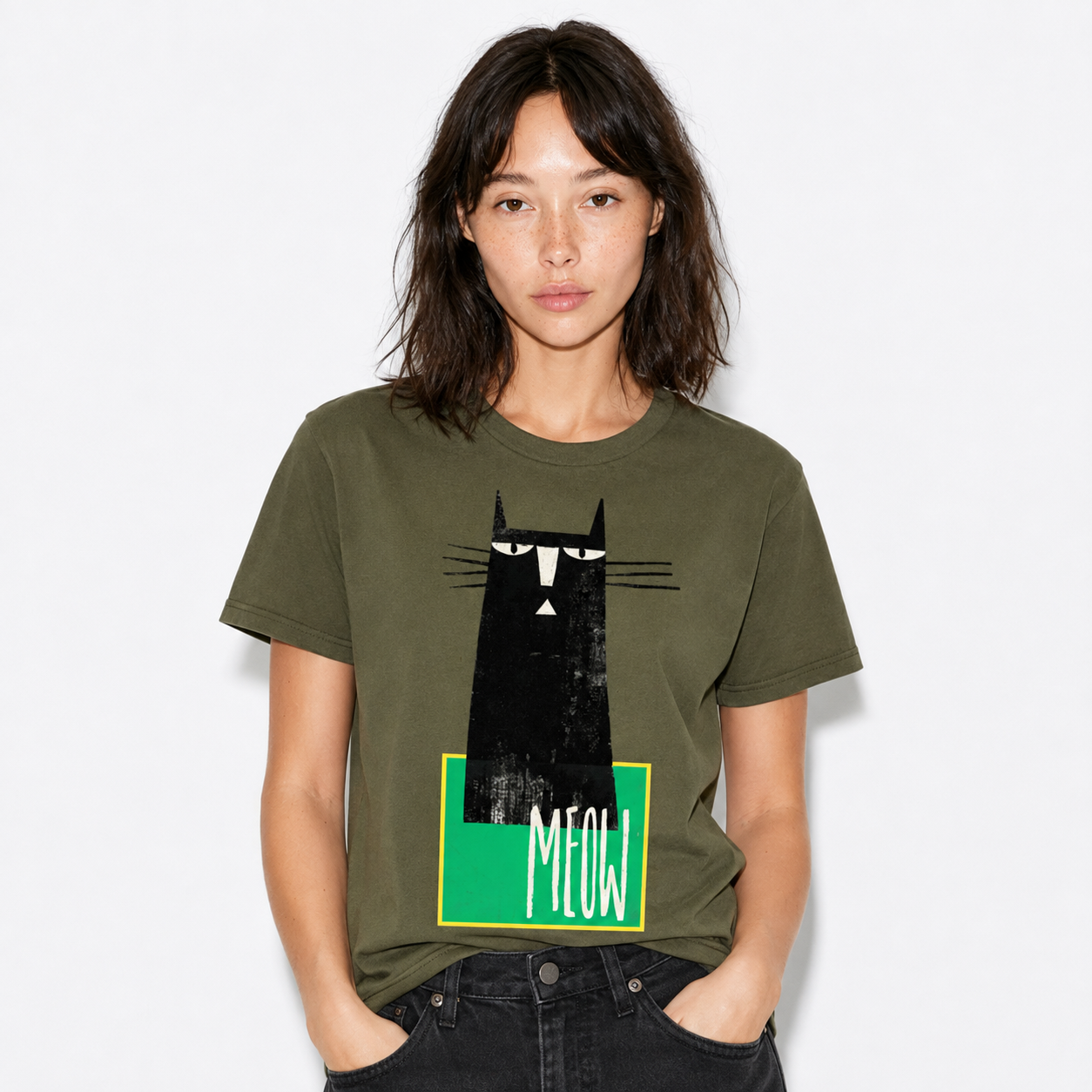 A woman wearing an olive green graphic t-shirt with a black cat illustration and the word 'MEOW' on a green block, paired with black jeans, against a light gray background.