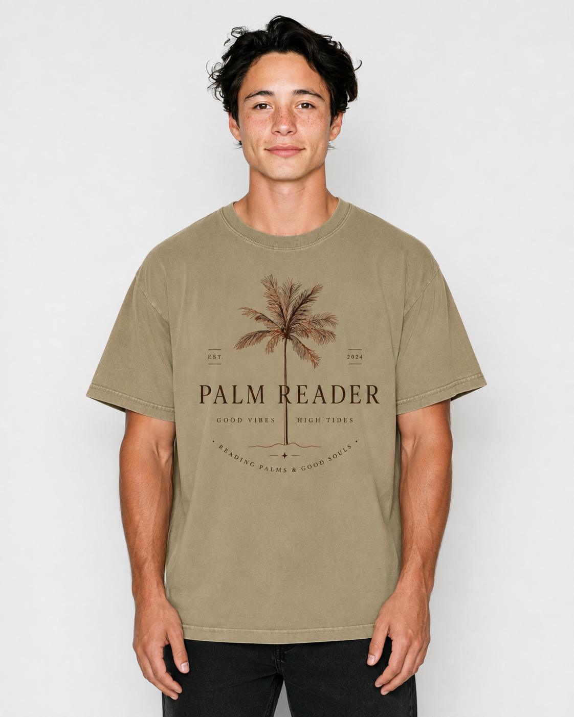 A man wearing a beige graphic t-shirt with a palm tree design and the text 'PALM READER' on the front, paired with black pants, set against a plain light gray background.