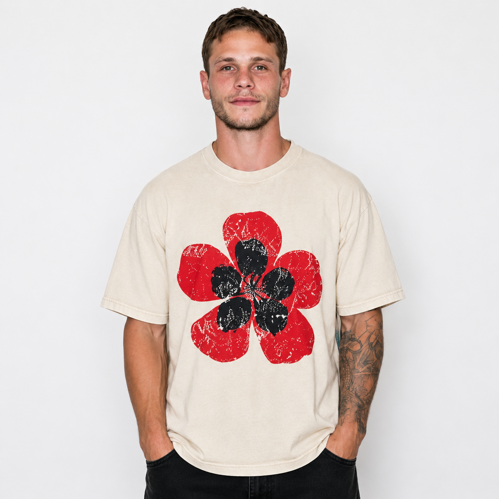 A man wearing a cream-colored t-shirt with a distressed red and black flower graphic on the front, set against a plain white background.