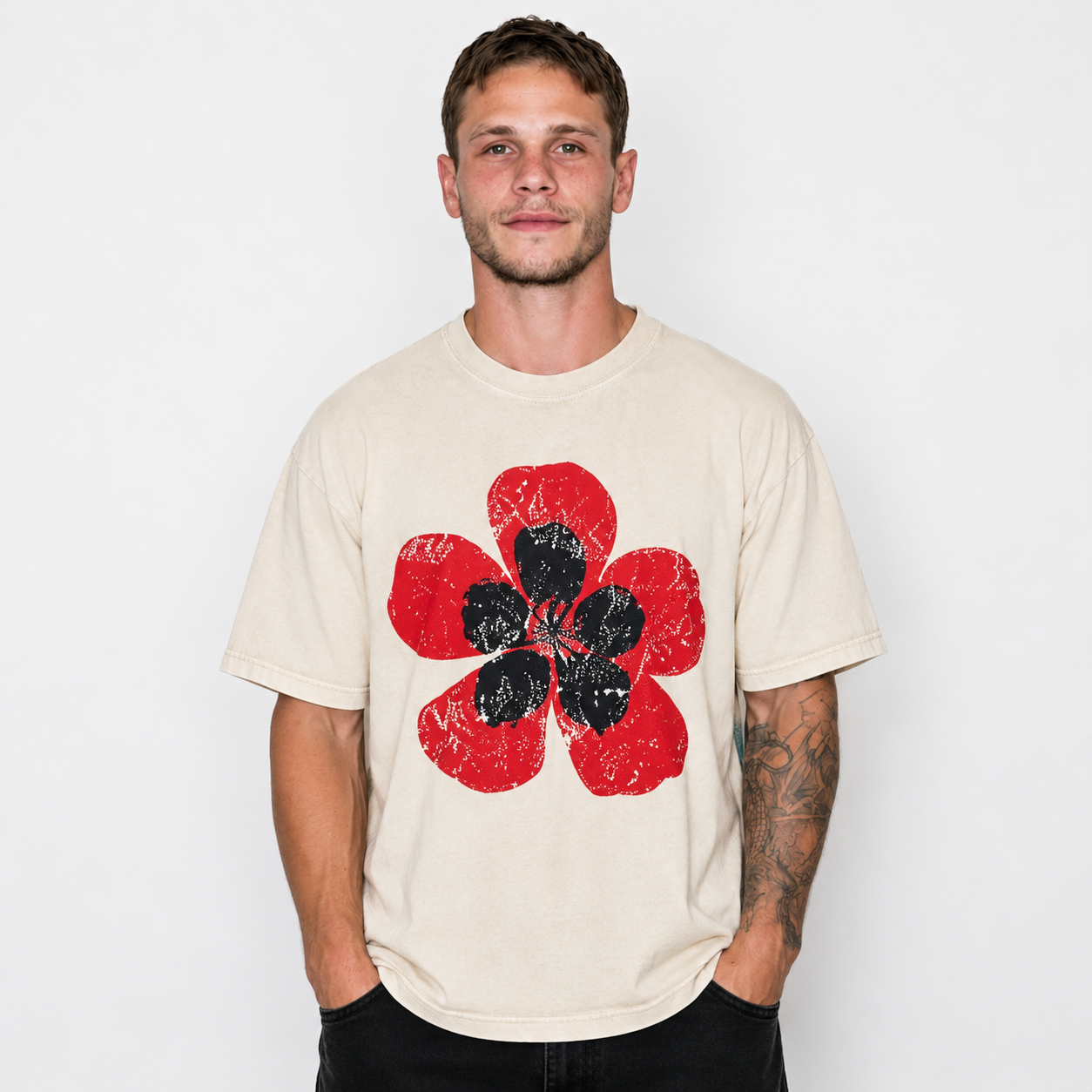 A man wearing a cream-colored t-shirt with a distressed red and black flower graphic on the front, set against a plain white background.