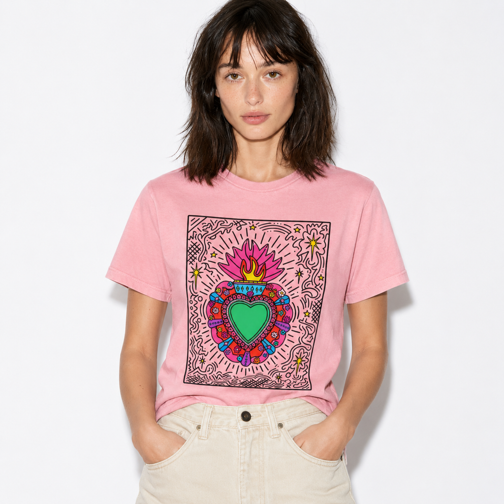 A woman wearing a pink graphic t-shirt with a colorful Sacred Heart design, paired with light beige jeans, against a plain white background.