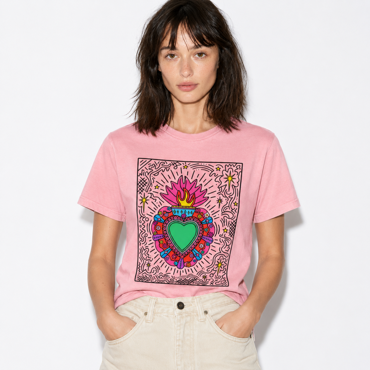 A woman wearing a pink graphic t-shirt with a colorful Sacred Heart design, paired with light beige jeans, against a plain white background.