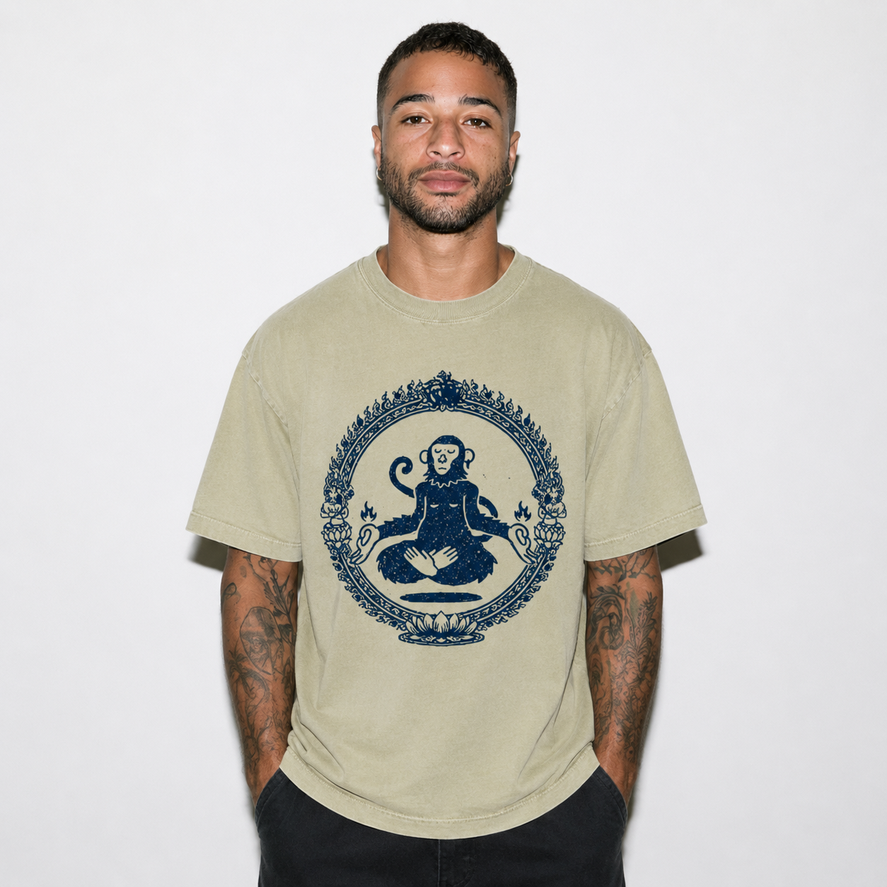 A man wearing a beige crewneck t-shirt with a dark blue graphic of a seated monkey inside an ornate circular frame, set against a plain white background.