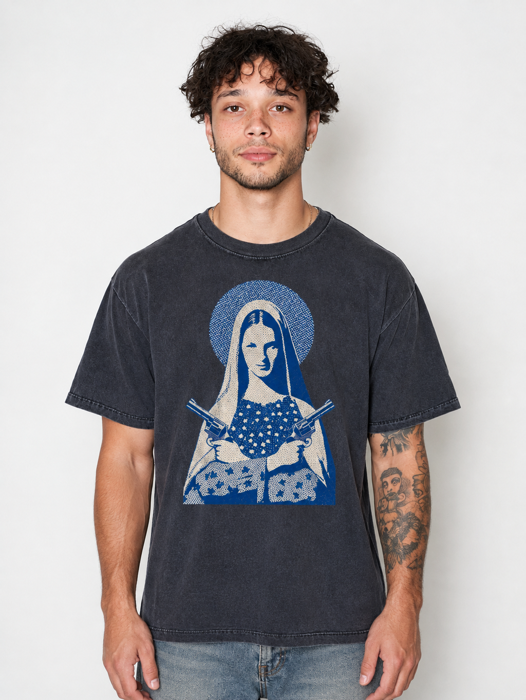A man wearing a faded black graphic t-shirt featuring a blue and white illustration of a robed figure holding swords, paired with light wash blue jeans, against a plain light gray background.