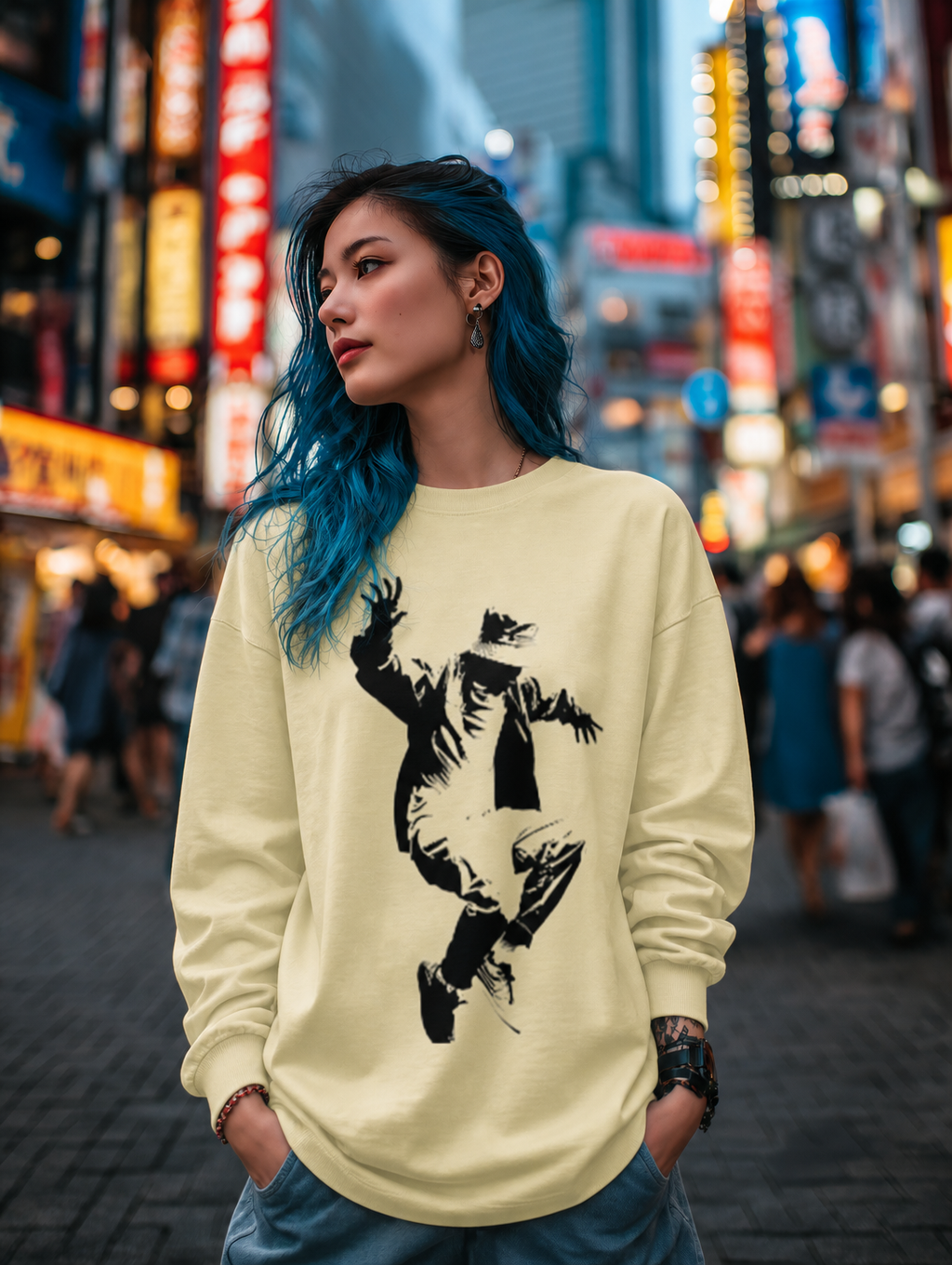 Person wearing a light yellow sweatshirt with a graphic design in a city street at night.