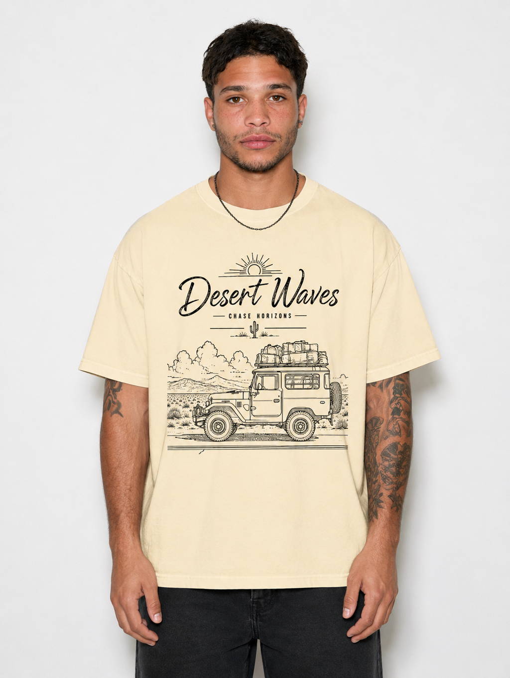 A man wearing a cream-colored graphic t-shirt with a black line art design of a vintage camper van and the text 'Desert Waves - Gravel Versions'.