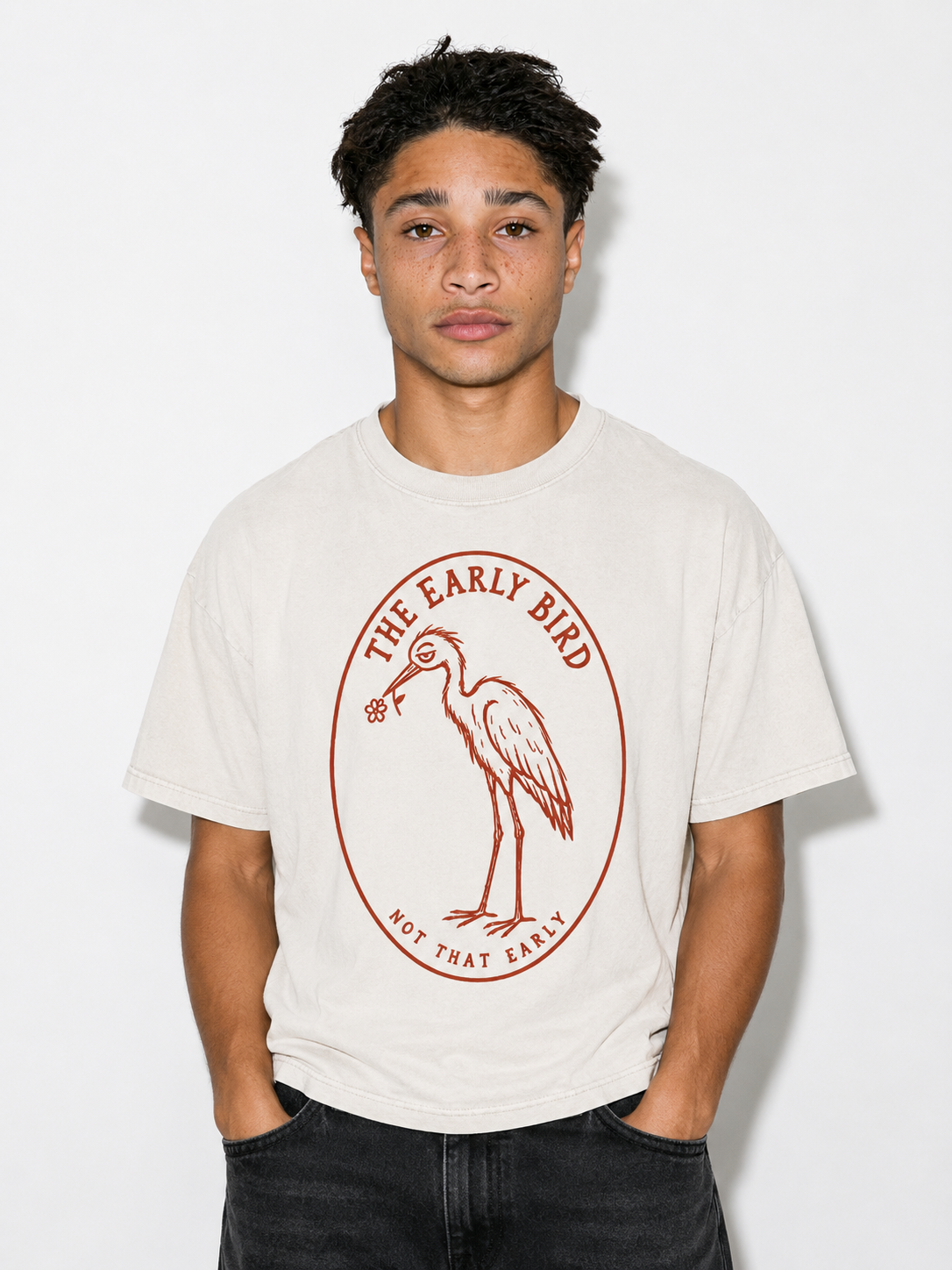 A young man wearing a cream-colored t-shirt with a red graphic of a heron inside an oval, with the text 'THE EARLY BIRD' and 'NOT THAT EARLY'.