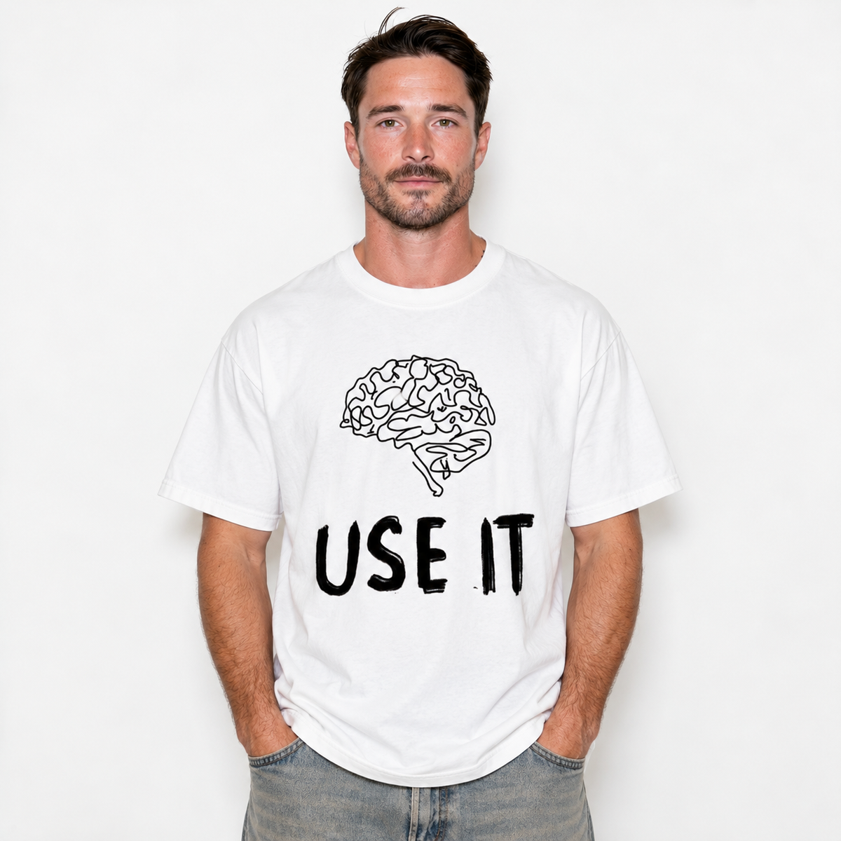 A man wearing a white crewneck t-shirt with a black line art graphic of a brain and the text 'USE IT' printed on the front, paired with gray jeans, against a plain white background.